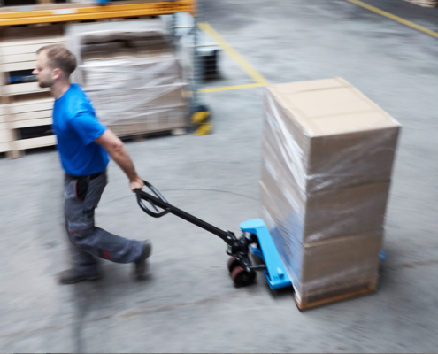 man pushes blue pallet truck into storage