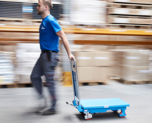 man pushes blue lift table into storage