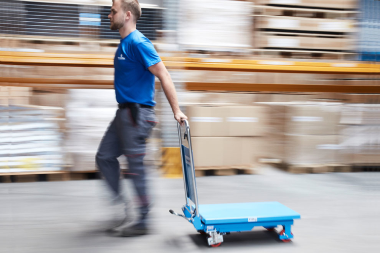 man pushes blue lift table into storage