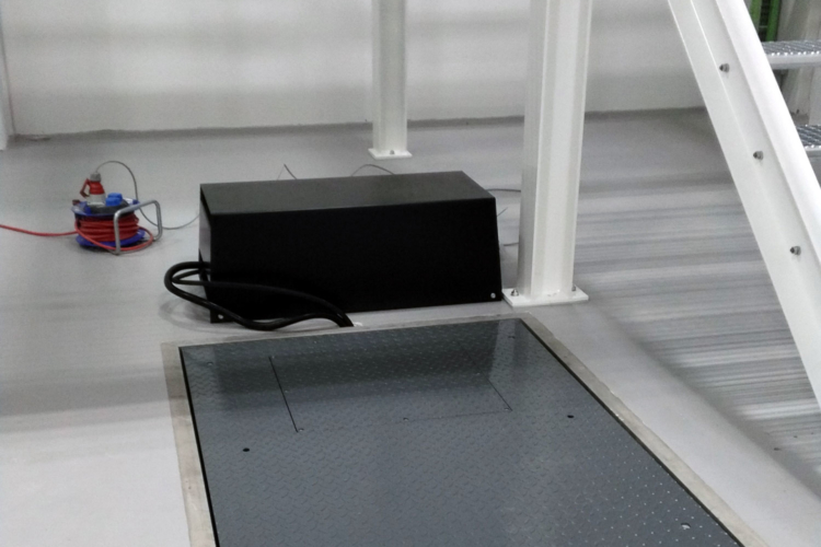 Versenkter Hubtisch im geschlossenen Zustand mit angeschlossener Antriebseinheit Bodenseitig geschlossener Scherenhubtisch mit sichtbarer Antriebseinheit und Elektroanschluss in Industrieumgebung.